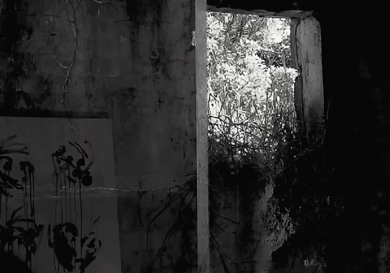 an abandoned concrete structure. There is a fresh artwork leaning against the wall. It is an artwork of dripping ink and fluid gesture. There are plants taking over the structure and pushing their way through the doorless entrance.