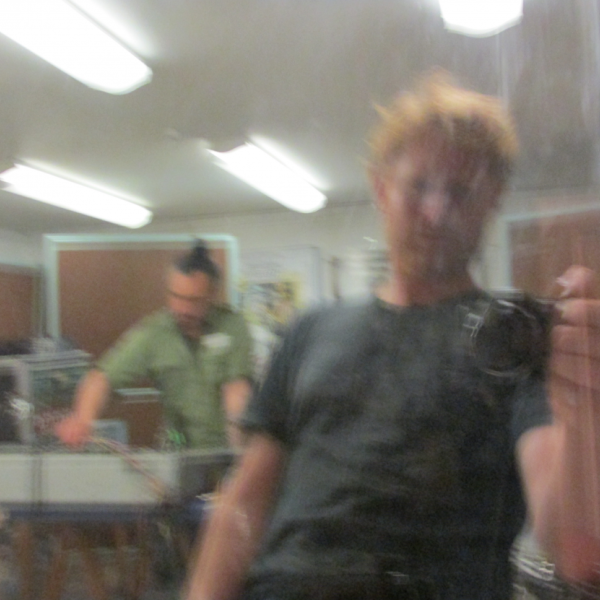 a blurry camera selfie featuring Dan Beban with a camera with Riki Gooch in the background