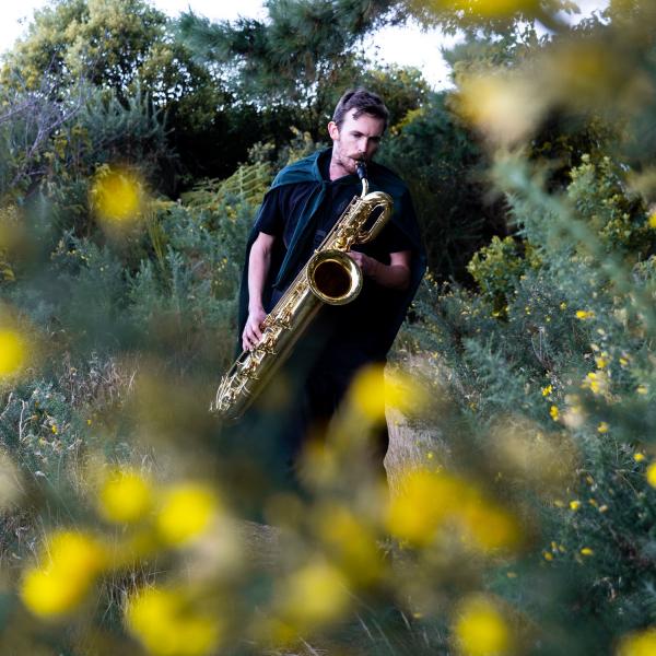 Jake Baxendale playing the saxophone in a bush 