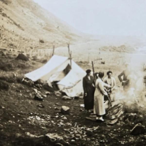 A sepia photo of people next to a tent in the mountains