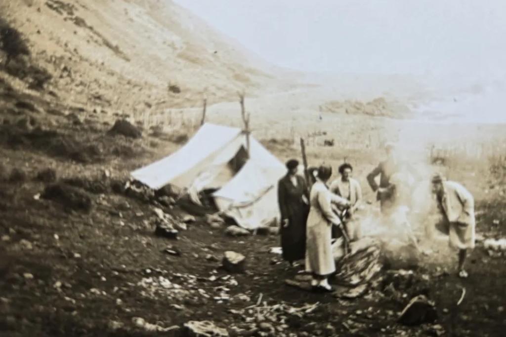 A sepia photo of people next to a tent in the mountains