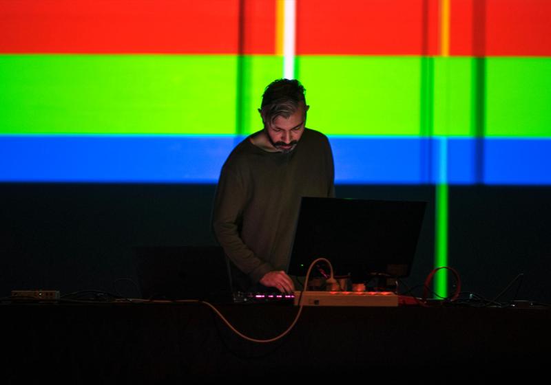 mHz playing in front of a backdrop of thick bright stripes of primary red, green, and blue