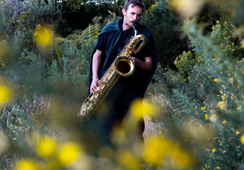 Jake Baxendale playing the saxophone in a bush 