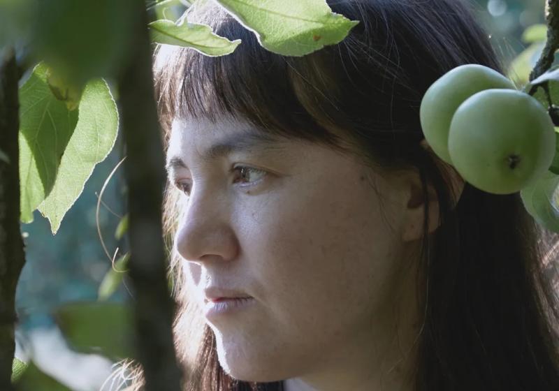 A close up of Delphine Dora amongst greenery looking calmly into the distance