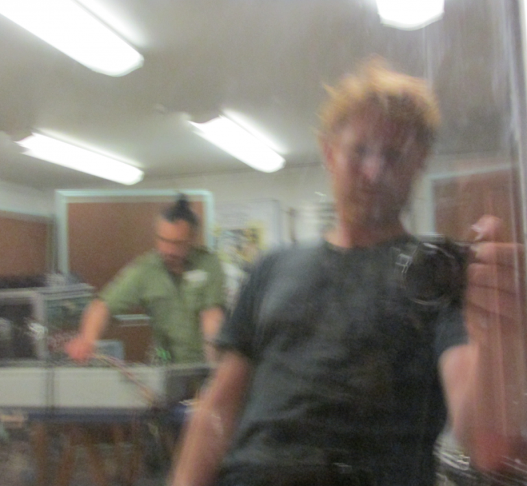 a blurry camera selfie featuring Dan Beban with a camera with Riki Gooch in the background