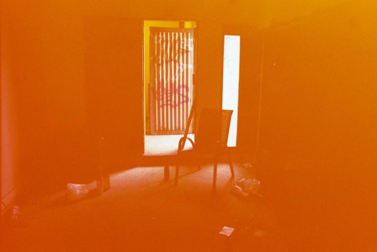 photo of a chair centred in a dark room with light reflecting from windows. photo is saturated in orange/red tones