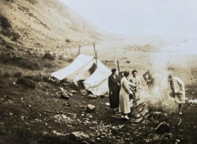 A sepia photo of people next to a tent in the mountains