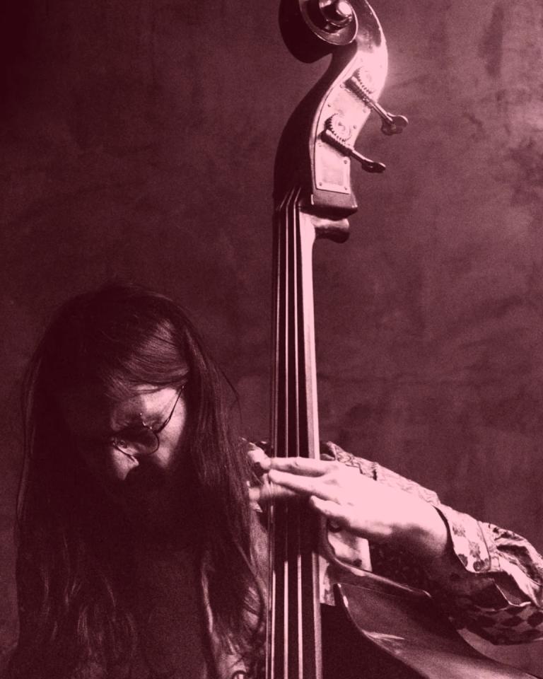A moody black and white dim-lit photo of Arturo playing the double bass
