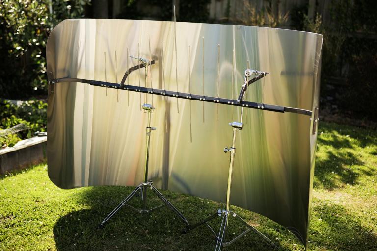 a large sheet of metal is bent into a curve. Inside the curve is a crossbeam with vertical steel bars of different lengths.